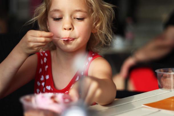 Elementary aged girl in a red polka dot top eating ice cream.