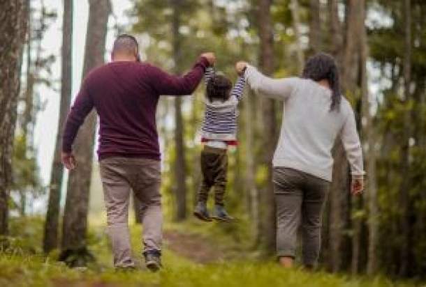 A man and woman swinging a young child between them while walking in the woods.