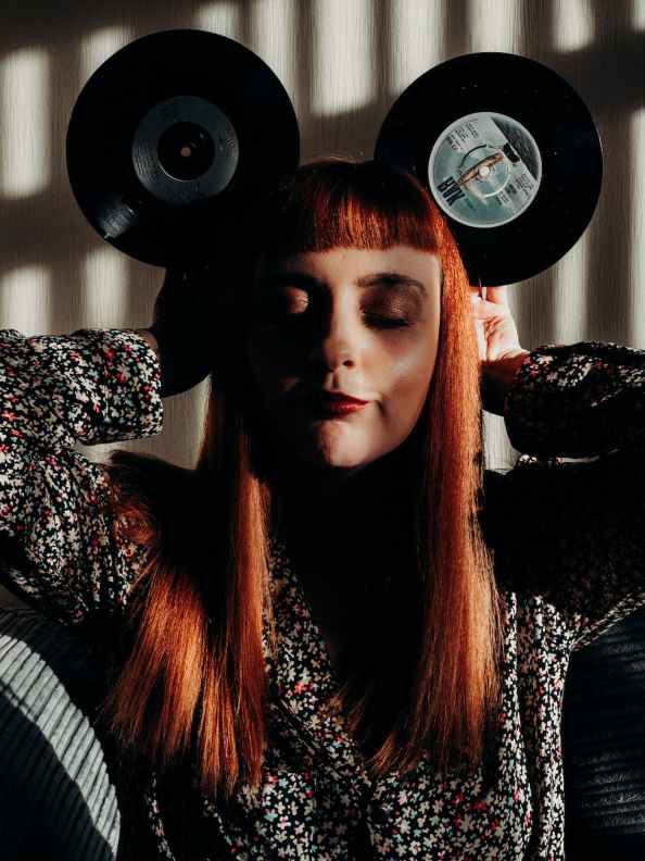 red hair woman with closed eyes holding vinyl records as mouse ears